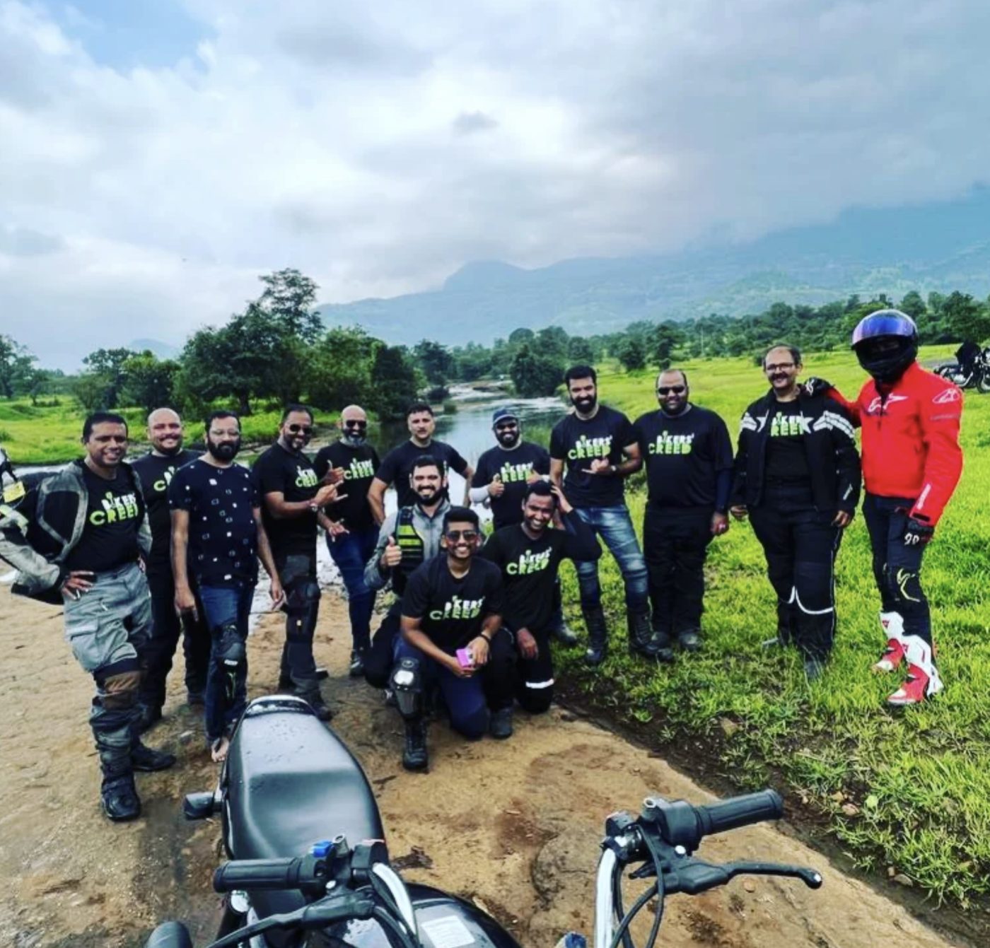 Riders from the Bikers Creed motorcycle club in their black club tees, posing beside a river with hills behind them